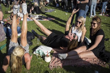 Amsterdam, Hollanda - 3 Temmuz 2016: Roots Open Air festivali sırasında çimlerin üzerinde oturan ve tezahürat eden bir grup genç kadın, Oosterpark Amsterdam'da ücretsiz halka açık etkinlik