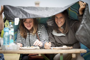 Amsterdam, Hollanda - 5 Temmuz 2015: Amsterdam Roots Open Air'de yağmur altında öğle yemeği alan 2 genç kadın, Park Frankendael'de 05/07/2015 tarihinde kültürel bir festival düzenlendi