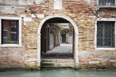 İtalya 'da Venedik' te bir kanalın yanındaki turuncu tuğla binanın küçük arka kapısı.
