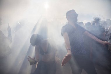 Amsterdam, Hollanda - 30 Temmuz 2017: Westerpark'taki Milkshake Festivali'nde güneşin parıldayarak duman içinde dans eden insanların silueti