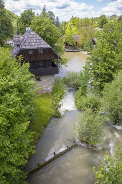 Ağaçlar ve bir şelale ile yeşil bir manzara ahşap evler ile bir nehir kanyon u Rastoke Hırvat köyü, Hırvatistan