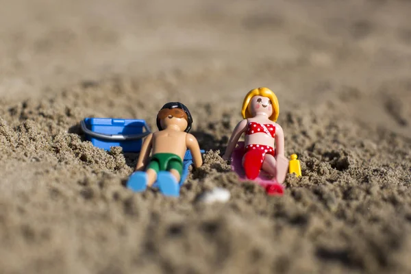 Amsterdam, the Nertherlands. April 12 3, 2015. A man and a woman sun tanning on the sand. Playmobil toy line exist since 1975 and is produced by the German company Brandtaetter.