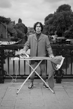 Amsterdam'da bir kanalın yanında, şehirde takım elbisesini ütüleyen adam.