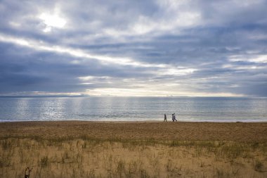 bulutlu bir kış günü gün batımında sahilde dolaşan bir grup insan