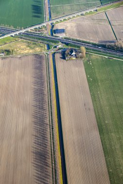 Hollanda'da bir çiftlik evi, kanal ve otoyol yolu ile yeşil alanların havadan görünümü.