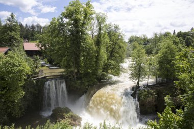 Ağaçlar ve bir şelale ile yeşil bir manzara ahşap evler ile bir nehir kanyon u Rastoke Hırvat köyü, Hırvatistan