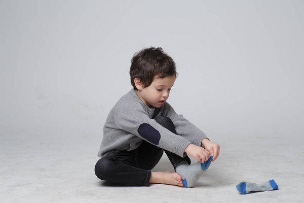 Portrait of Cute little kid sitting  learning how to put the socks on by him self, Happy Toddler boy pulling his socks to his foot, Child development concept