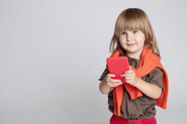 Akıllı telefon tutan bir çocuk. Bir tane. Çevrimiçi öğrenme, karantina, cihazlar, internet. Ön manzara. Oğlanın saçları kalın, kırpık değil. Uzayı kopyala Yatay olarak. Gri arka plan. Stüdyo ışığı. Portre.