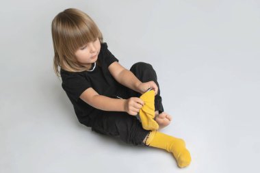 Küçük şirin çocuk kendi başına çorapları giymeyi öğreniyor. Çocuk ayağına çorap çekiyor. Çocuk becerileri geliştirme konsepti. Uzayı kopyala Kafkasyalı. Uzun saçlı bir çocuk.. 