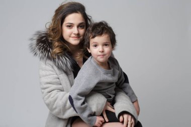 Erkek ve kız kardeşler gri arkaplanda bu kavramsal resimde neşeli bir şekilde poz verirler. Kardeş dostluğu kavramı. Farklı yaşlardaki çocuklar.