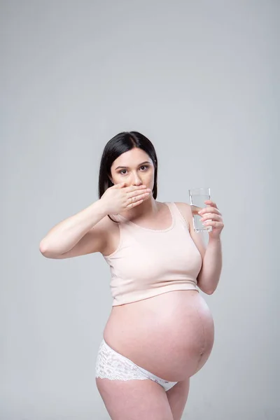 怀孕的女人穿着内裤 手里拿着一杯水 情感工作室在白色背景下拍摄怀孕的照片 喝还是不喝 怀孕最后一个月 你看杯子里有酒保健概念 — 图库照片