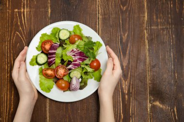 Yuvarlak tabakta taze sebze salatası. Koyu ahşap arka plan. Sağlıklı yemek konsepti, keto diyeti, düşük kalorili yemekler. Adamın elleri masaya doğranmış sebzeli beyaz bir tabak koydu. Lezzetli.