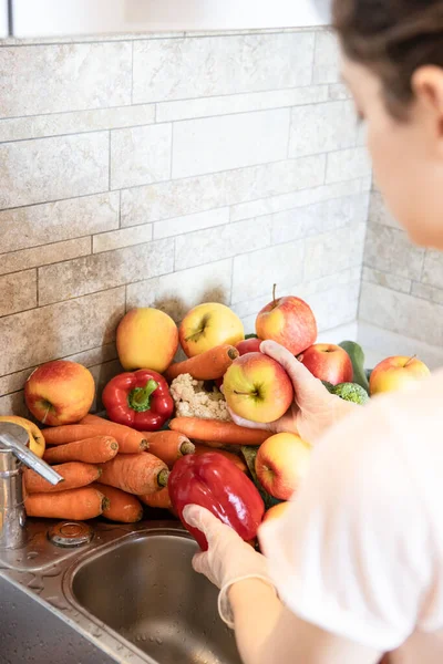 Concept of hygiene, pandemic sanitation, vitamins, prevention, stay healthy. Hands in rubber gloves wash pepper under tap, running water. Lifestyle. Bright colors. Vegetables, fruits in the sink.