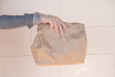Enfeksiyon önleme konsepti, salgın yaşam tarzı. Şeffaf lastik eldivenli bir insan tek eliyle bir el çantası tutar. Ön manzara. Güneş ışığı, dışarıda. Boşluğu kopyala. 