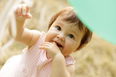 Sevimli, gülümseyen bir bebek bir ışık balonuna uzanır. Parmaklar ağızda. Üst Manzara. Açık havada. Kafkasyalı. Pozitif duygular, mutlu bebek. Doğum günü konsepti, çocuk koruması. Yaşam biçimi.
