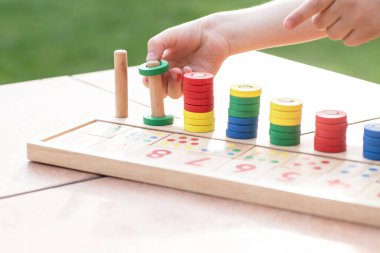 Çocuklar için matematik oyunu. Çocuk eli çok renkli yüzüklerle oynar. Doğal malzemeler, ahşap. Sayı, sayı kompozisyonu. Evde eğitim kavramı, erken gelişim, yetenekler. Gün ışığı. Dışarıda..