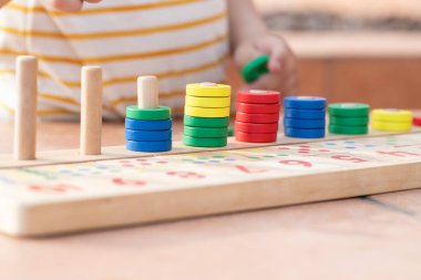 Beyaz sarı çizgili tişörtlü bir çocuk saymayı öğreniyor. Matematik oyuncağı. Çocuk eli çok renkli yüzükler takar. Doğal malzemeler, ahşap. Erken gelişim, beceri kavramı. Gün ışığı dışarıda..