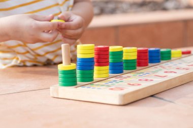 Beyaz sarı çizgili tişörtlü bir çocuk saymayı öğreniyor. Matematik oyuncağı. Çocuk eli çok renkli yüzükler takar. Doğal malzemeler, ahşap. Erken gelişim, beceri kavramı. Gün ışığı dışarıda..