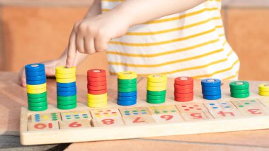 Çocuklar için matematik oyunu. Çocuk eli çok renkli yüzüklerle oynar. Doğal malzemeler, ahşap. Sayı, sayı kompozisyonu. Evde eğitim kavramı, erken gelişim, yetenekler. Gün ışığı. Dışarıda..
