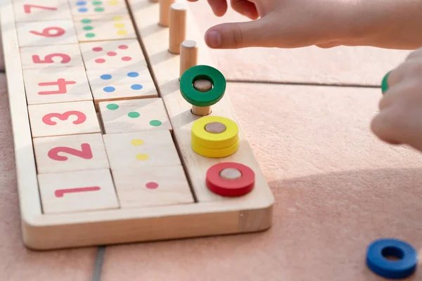 Çocuklar için matematik oyunu. Çocuk eli çok renkli yüzüklerle oynar. Doğal malzemeler, ahşap. Sayı, sayı kompozisyonu. Evde eğitim kavramı, erken gelişim, yetenekler. Gün ışığı. Dışarıda..