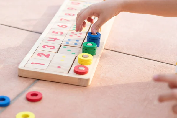 Çocuklar için matematik oyunu. Çocuk eli çok renkli yüzüklerle oynar. Doğal malzemeler, ahşap. Sayı, sayı kompozisyonu. Evde eğitim kavramı, erken gelişim, yetenekler. Gün ışığı. Dışarıda..