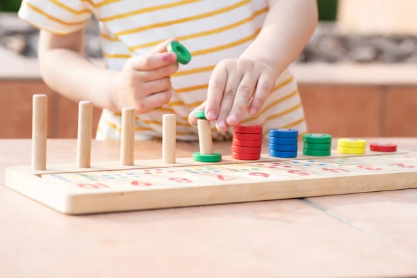 Beyaz sarı çizgili tişörtlü bir çocuk saymayı öğreniyor. Matematik oyuncağı. Çocuk eli çok renkli yüzükler takar. Doğal malzemeler, ahşap. Erken gelişim, beceri kavramı. Gün ışığı dışarıda..