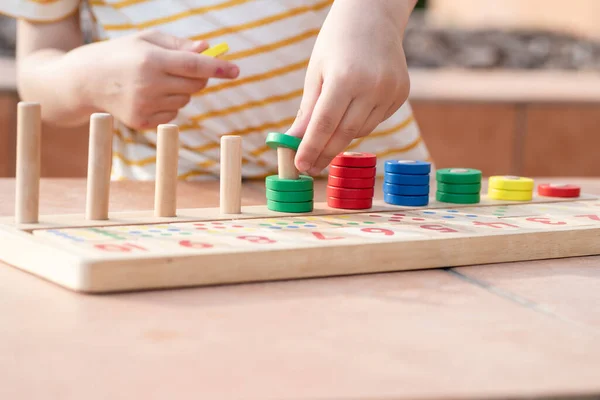 Beyaz sarı çizgili tişörtlü bir çocuk saymayı öğreniyor. Matematik oyuncağı. Çocuk eli çok renkli yüzükler takar. Doğal malzemeler, ahşap. Erken gelişim, beceri kavramı. Gün ışığı dışarıda..
