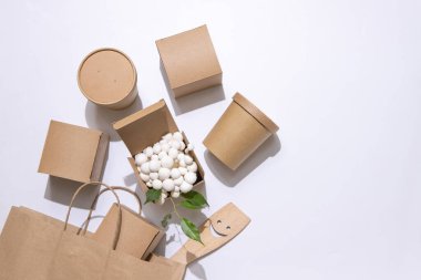 Teslimat konsepti, paket servisi, geri dönüşüm, olumlu duygular. Eşya kutuları, yiyecek poşetleri, içecekler. Açık bir kabın içinde, küçük mantarlar ve yeşil yapraklar. Mutfak ahşap spatulası. Beyaz arka plan. Üst görünüm.