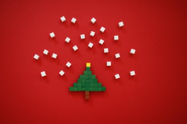 Minimalist Noel kartı. Mutlu bir yeni yılın sembolü. Noel ağacı, kırmızı arka planda kar taneleri. Yaratıcı kompozisyon çok renkli çocukların ahşap piksellerinden oluşur. Yatay olarak. Boşluğu kopyala