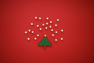 Minimalist Noel kartı. Mutlu bir yeni yılın sembolü. Noel ağacı, kırmızı arka planda kar taneleri. Yaratıcı kompozisyon çok renkli çocukların ahşap piksellerinden oluşur. Yatay olarak. Boşluğu kopyala