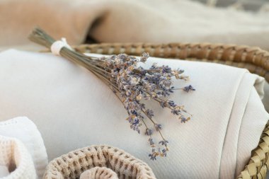 Rahat bir ev için dekorasyon. Güzel eşyalar. Yuvarlak havlu, katlanmış bej kumaş, sepetteki lavanta buketi. Kapatın. Hiç kimse. Yatay olarak. Kokular, spa, provence tarzı.