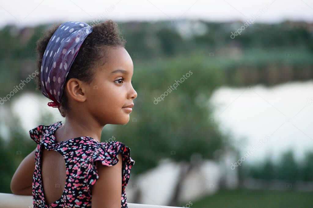 Photo at sunset. The child against the background of the landscape. Portrait. Mixed race person, afro hair. The concept of happiness, stop racism, vacation, life, nature.