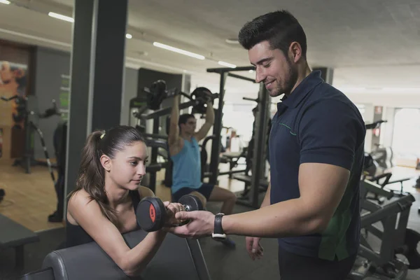 Coach training young woman lifting weights at gym