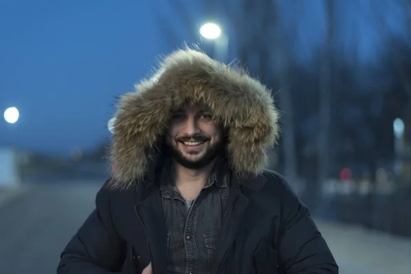 man with fox fur parka coat poses during the blue hour on a winter night