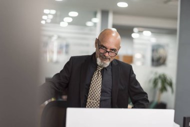 Üst düzey kel adam kamera bakarak ve poz siyah takım elbise ile ofiste çalışan 