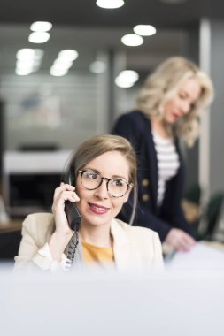 Çekici 30s kadın telefon ve arka planda diğer ofiste çalışan