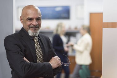 üst düzey adam portre ofis takım elbise, blurowner, arka planda insanlar ile gülümseyerek poz