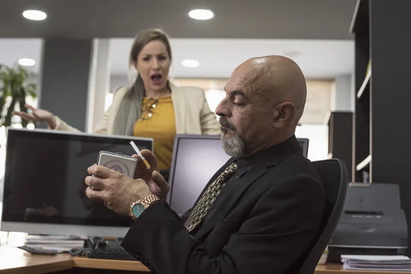 senior suit man ready for smoke cigar in workplace and angry woman nagging his attitude