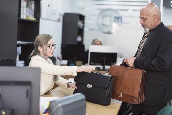 Mature man and young woman with briefcases in office symbolizing changing generations and equality of sex in employment.