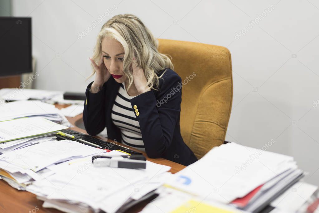 Female office worker stressed before a large load of documents and office work