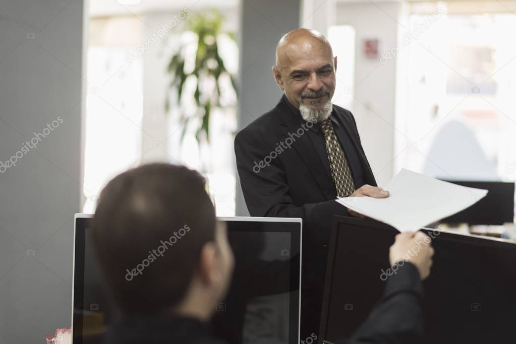 Mature boss taking paper from employee at office workplace of insurance company