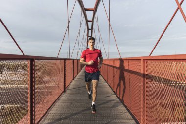 Gün batımında kırmızı köprüde koşan kırmızı lı adam