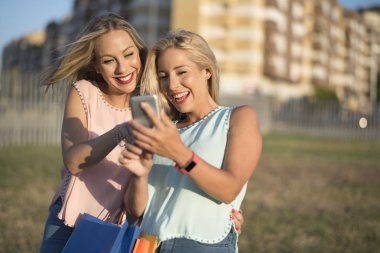Şehir parkında iki kardeş kadın şehir parkında gülümseyerek akıllı telefon arıyor