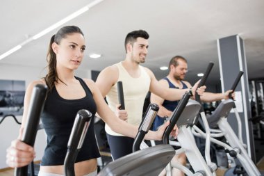 Spor salonunda egzersiz eliptik eğitmen genç kadın ve erkek ile Grup