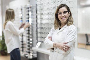 Gözlük mağazasında poz veren optometrist kadına gülümseyerek bakıyor 