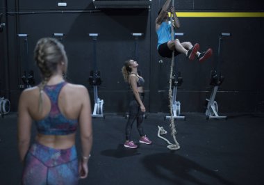 Genç adam spor salonunda ipe tırmanıyor.