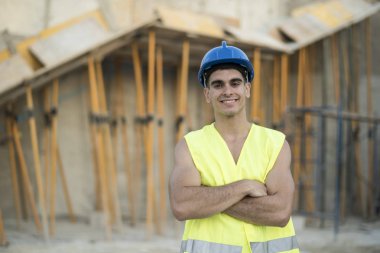 İnşaat işçisi poz ve kamera bakıyor, şantiyede gülümseyerek