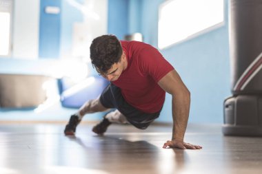Genç bir adam spor salonunda şınav çekmeyi öğreniyor.