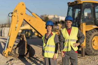 Arka planda ağır vasıta ile kameraya bakan portre pozinşaat inşaat işçileri