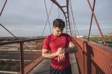 Gün batımında kırmızı köprüde çalışan ve akıllı saat görünümlü kırmızı adam